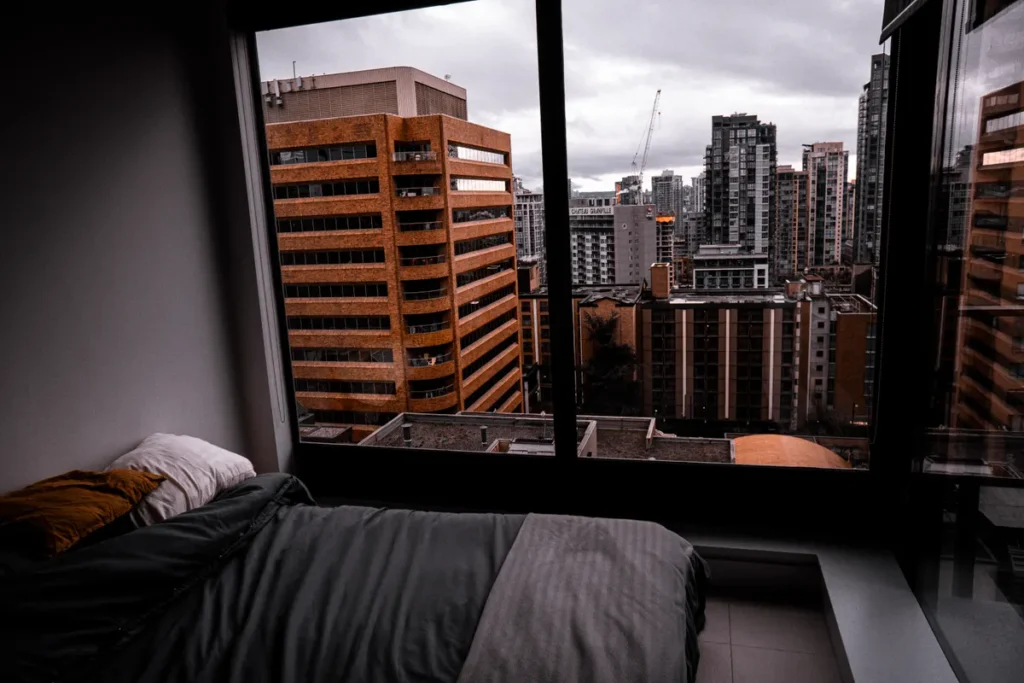 Quarto com janela ampla voltada para prédios da cidade